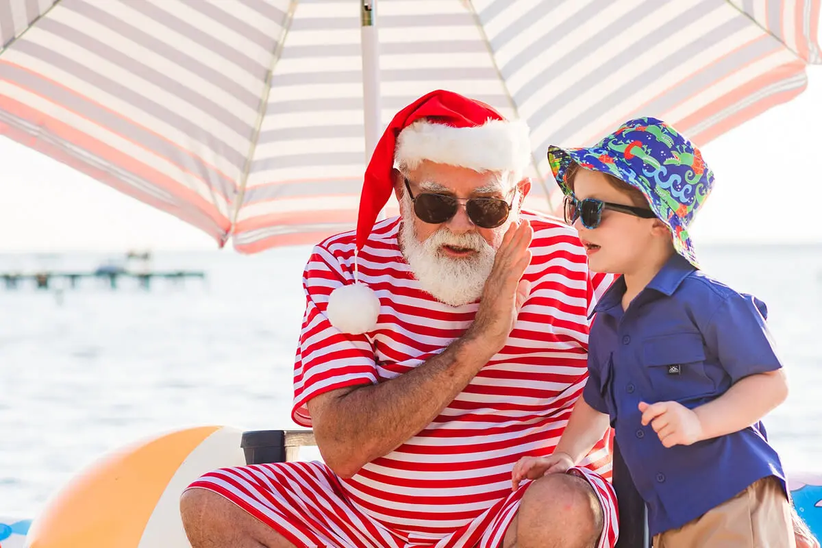 Santa and child sharing secrets on beach.