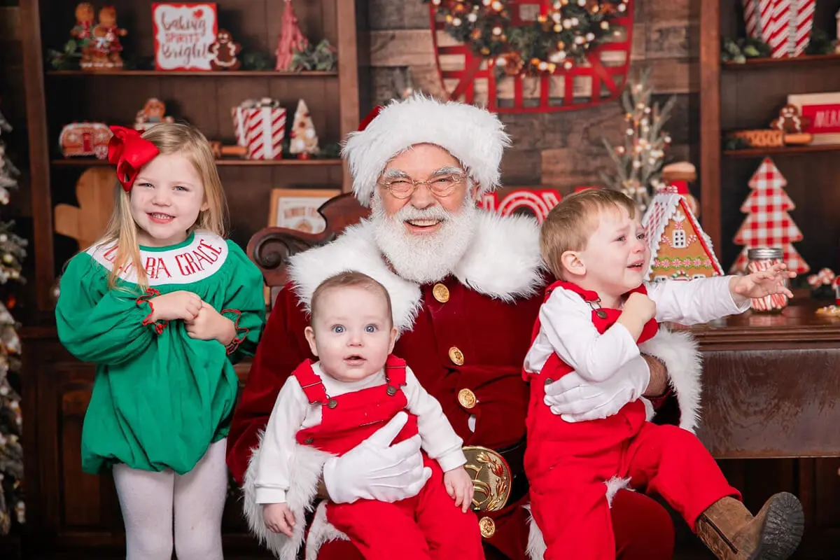 Santa with three smiling children in Christmas setting.