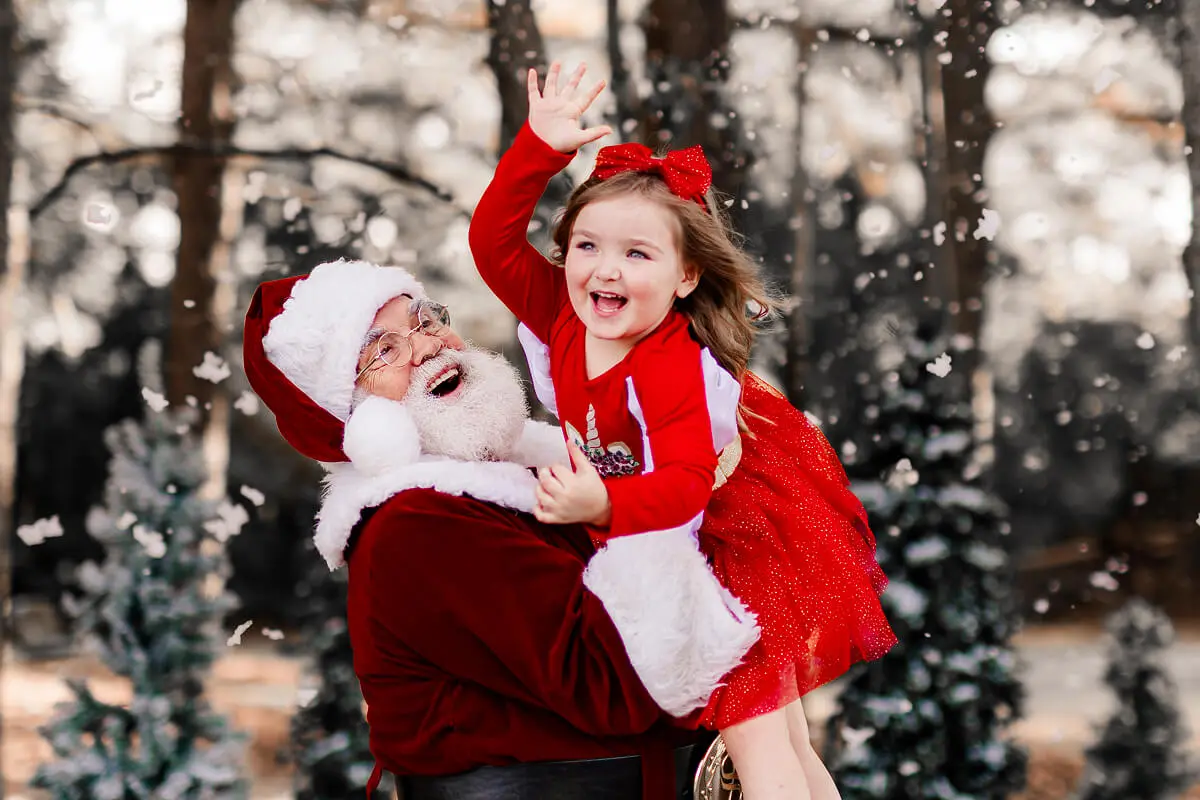 Santa holding joyful child in snowy forest.