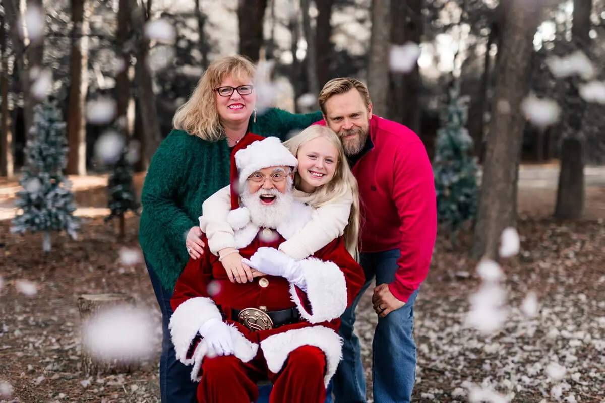 Family posing with Santa in snowy forest.